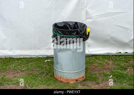 A metal rubbish bin with a black bag in it outside a white marquee on grass. Stock Photo