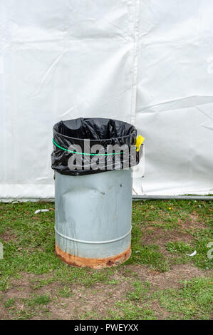 A metal rubbish bin with a black bag in it outside a white marquee on grass. Stock Photo