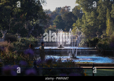 Sun glinting on two fountains in pools in the Italian Garden in Kensington Gardens, London,UK in the fall. Lush vegetation surrounds the tranquil area Stock Photo