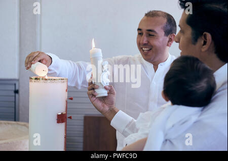 MERIDA, YUC/MEXICO - NOV 18, 2018: Godfathers light up their baptism candles during the ceremony at a catholic church. Goddaughter in arms. Stock Photo