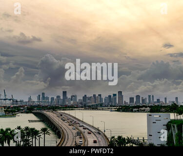 Dark storm clouds loom over downtown Miami at sunset as a constant flow of traffic crosses the MacArthur Causeway to Miami Beach