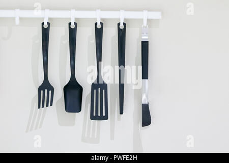 Black kitchen utensils hanging on white wall with copy space Stock Photo
