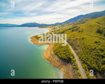 Rural road winding along shore of Blowering Reservoir - aerial view Stock Photo