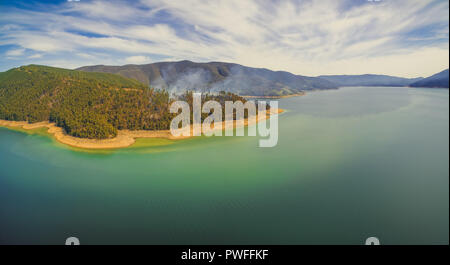 Aerial panorama of smoke rising from forest on beautiful lake shore Stock Photo