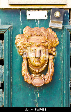 Old rusty  vintage door knocker with a face on a green wooden door with chipped paint. Stock Photo