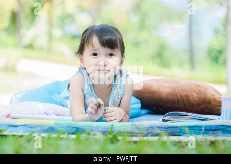 Little girl lying with drawing book on mat in park with happy face when her relaxant in morning holiday Stock Photo