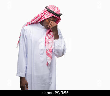 Young arabic african man wearing traditional keffiyeh over isolated background tired rubbing nose and eyes feeling fatigue and headache. Stress and fr Stock Photo