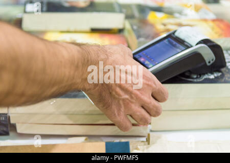 Close up of male hand using credit card swiping machine to pay. Man entering credit card code in POS machine in a book store. Stock Photo