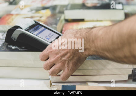 Close up of male hand using credit card swiping machine to pay. Man entering credit card code in POS machine in a book store. Stock Photo