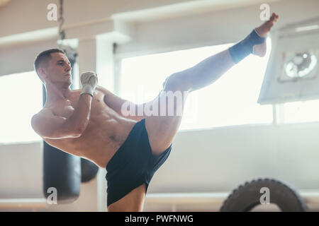 Muay thai boxer doing high kick. Young athlete demonstrates kickbox. Stretching and balance concept Stock Photo