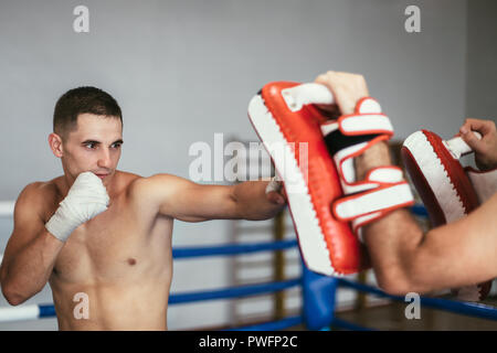 Kickboxer training with partner in boxing paws, using boxing mitts. Preparing for competition Stock Photo