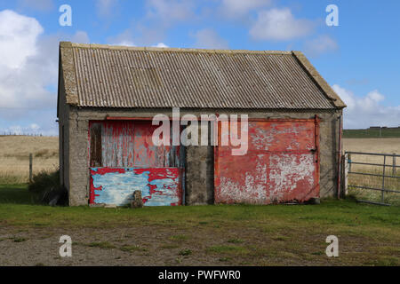 Derelict two door garage in Orkney Mainland, Scotland, that had been boarded up with plywood,its brightly colored paint was peeling off. Field,bluesky Stock Photo