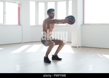 Handsome Young Man Doing Squad With Medicine Ball As Part Of Bodybuilding Training Stock Photo