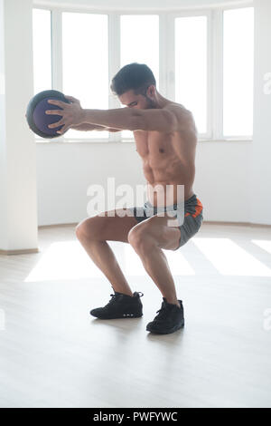 Handsome Young Man Doing Squad With Medicine Ball As Part Of Bodybuilding Training Stock Photo