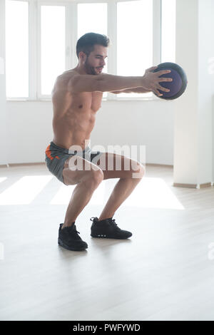 Handsome Young Man Doing Squad With Medicine Ball As Part Of Bodybuilding Training Stock Photo