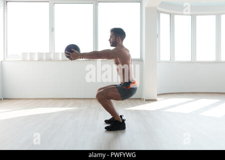 Handsome Young Man Doing Squad With Medicine Ball As Part Of Bodybuilding Training Stock Photo