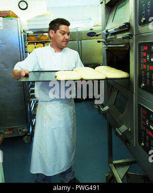 Baker placing dough bread in oven. Stock Photo