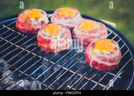 Making home made Beer Can Bacon Burgers on barbecue grill. Preparing stuffed patties, wrapped  in bacon and grilling on indirect heat in nature at bac Stock Photo