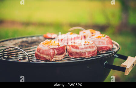 Making home made Beer Can Bacon Burgers on barbecue grill. Preparing stuffed patties, wrapped  in bacon and grilling on indirect heat in nature at bac Stock Photo