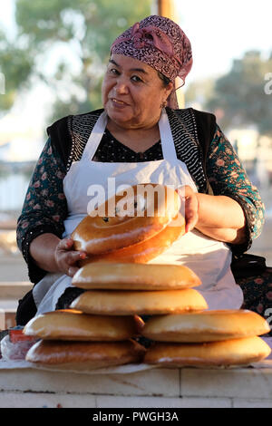 A vendor with capped gold teeth selling traditional Bukhara-style non or naan oven-baked flatbread in Siyob Bazaar also called Siab Bazaar, the largest bazaar in the city of Samarkand alternatively Samarqand in Uzbekistan. Replacing natural teeth with gold implants or caps was once a status symbol and prestige in Uzbekistan and other countries of Central Asia. However, the younger generation seldom follows this tradition. Stock Photo