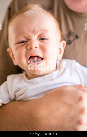 Father holding in right hand his crying, four months baby Stock Photo