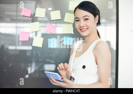 Asian business women smiling and working together on wall glass with post it stickers. Modern startup office Stock Photo
