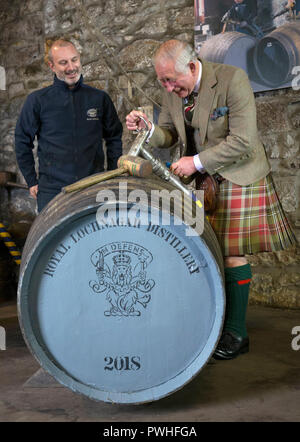 The Prince of Wales, known as the Duke of Rothesay while in Scotland, fills a new whisky cask, alongside senior operator Ryan Cromar, during a visit to the Royal Lochnagar Distillery at Crathie on Royal Deeside. Stock Photo