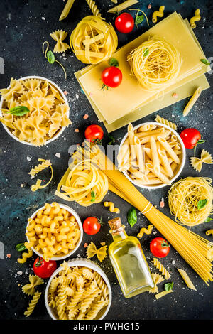 Italian food concept, various raw pasta assortment - spaghetti, lasagna, fusilli, tagliatelle, penne, tortellini, ravioli, with tomatoes and basil lea Stock Photo