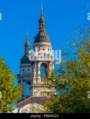 The domes of the architectural monument - St. Stephen's Basilica in Budapest. View of the church through the foliage of trees. Stock Photo