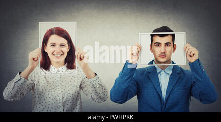 Businessman and woman covering their faces using photo sheets with happy and sad portrait emoticon, like a mask to hide the real emotion from society. Stock Photo