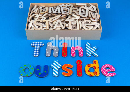 Think outside the box with a box full off dull mixed letters saying humdrum and static with a creative colourful patterned message on a blue backgroun Stock Photo