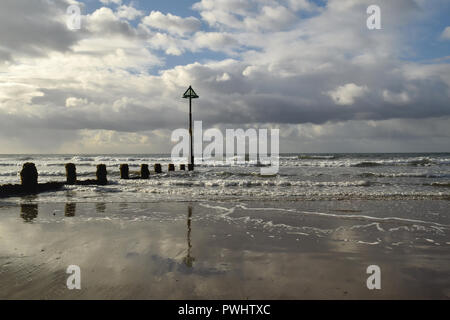 Groynes beach marker looking out to sea with cloudy blue sky between Ynyslas and Borth, Ceredigion, North Wales Stock Photo