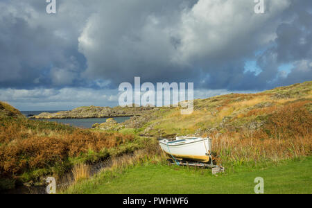 Scotland, small white fishing boat tied up on dry land in remote area of the Ardnamurchan peninsular in the Scottish Highlands. Heavy, cloudy skies.
