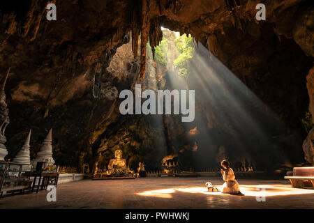 Woman worship the Buddha statue with sun light in the cave at Khaoluang,Phetchaburi Province, Thailand. This place is a public place. People have acce Stock Photo