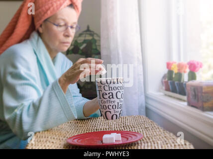 A mature lady who after her bath has a coffee. Unfortunately, she abuses sugar cubes. Stock Photo