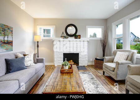 Spacious living room with traditional fireplace, grey sofa, two armchairs and wood coffee table. Stock Photo