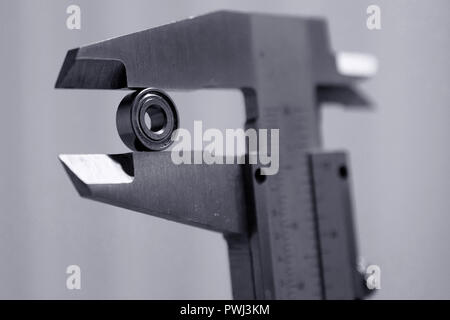 Measuring small bearing with vernier caliper. Monochrome close up image, shallow depth of field. Stock Photo