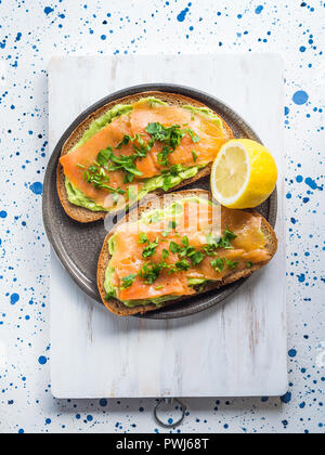 Rye bread avocado toasts with smoked salmon on white wooden board Stock Photo
