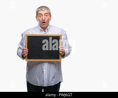 Handsome senior teacher man holding blackboard over isolated background scared in shock with a surprise face, afraid and excited with fear expression Stock Photo