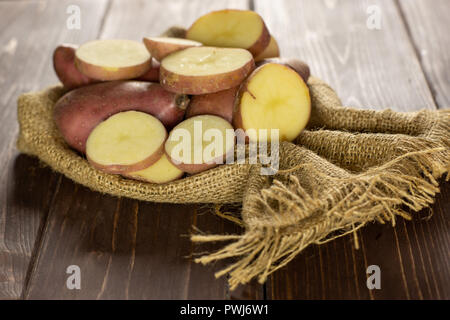 Lot of whole lot of slices of fresh red potato francelina variety on jute cloth on brown wood Stock Photo