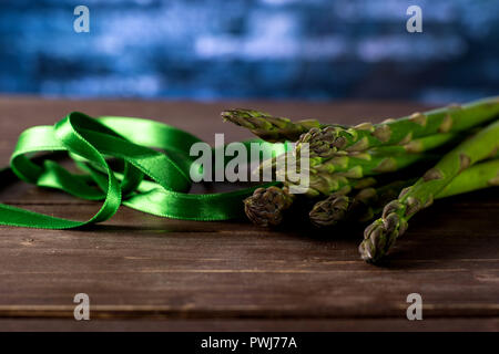 Lot of whole fresh green asparagus spear tied by green ribbon on brown wood Stock Photo