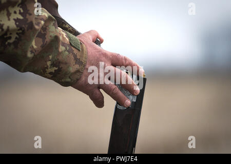 Man in a camo vest loading a gun during a hunting day Stock Photo