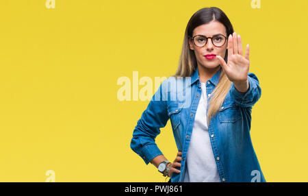 Young beautiful woman over wearing glasses over isolated background doing stop sing with palm of the hand. Warning expression with negative and seriou Stock Photo