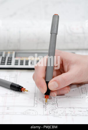 Woman's hand holding rapidograph, architectural plans in background Stock Photo