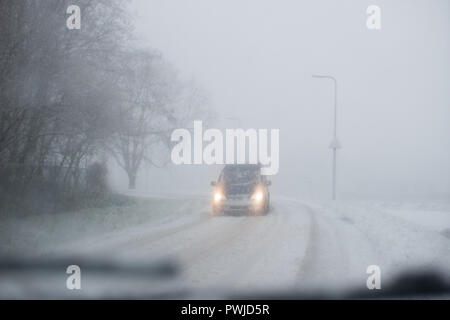 Car with lights on on a snowy road viewed from behind the windshield Stock Photo