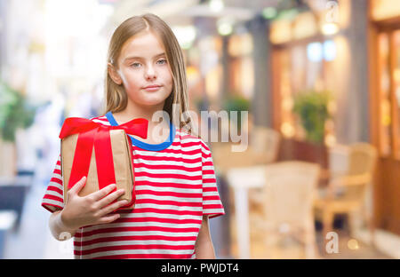 Young beautiful girl giving christmas or valentine gift over isolated background with a confident expression on smart face thinking serious Stock Photo