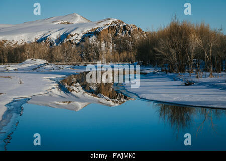 Snowy Mongolian landscape, reflection of snowy mountains,trees and blue sky in an icy river. Arkhangai, Mongolia Stock Photo