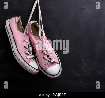 pair of pink textile sneakers hanging on a lace on a black background, copy space Stock Photo