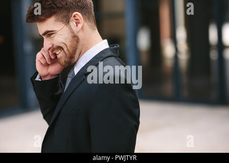 Smiling businessman talking over cell phone. Side view of business professional looking busy talking on mobile phone outdoors. Stock Photo
