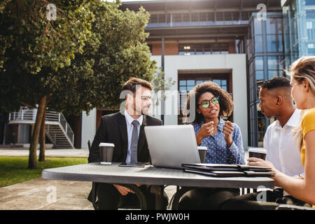 Female executive explaining new business strategy to team while sitting outdoors at table. business professionals discussing work at office cafeteria. Stock Photo